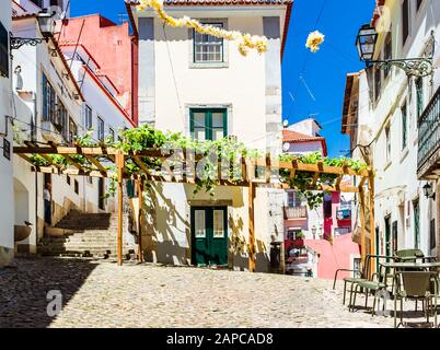 Piccola piazza acciottolata decorata con baldacchino in legno e vigneti nel quartiere di Alfama in una soleggiata giornata primaverile. Foto Stock