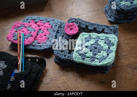 quadretti di granny crochet fatti a mano con ganci a crochet su tavolo di legno. Foto Stock