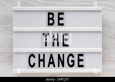 Parole 'essere il cambiamento' su un lightbox su una superficie di legno bianco, vista dall'alto. Sopra, dall'alto, disposizione piana. Foto Stock