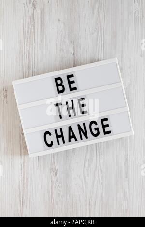Parole 'essere il cambiamento' su un lightbox su uno sfondo bianco di legno, vista dall'alto. Sopra, dall'alto, disposizione piana. Foto Stock