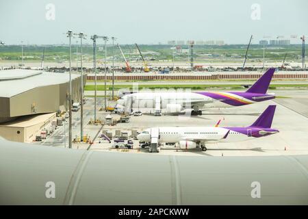 La vista dell'aeroporto è affollata, con aerei alle porte e decollo, camion tutto intorno e tramonto sullo sfondo. Viaggi e concetti di settore. Foto Stock