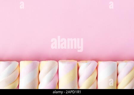 Fila di dolci marshmallows multicolore su sfondo rosa pastello. Primo piano deliziosi dolci morbidi. Disposizione piatta con spazio di copia. Vista dall'alto. Foto Stock