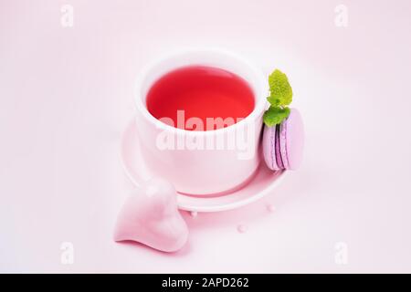 Tè alla frutta, blackberry macaroon o macaron e cuore di ceramica rosa su sfondo rosa pallido, copia spazio Foto Stock