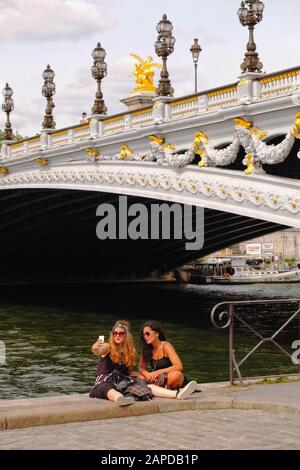 Due donne fanno un selfie sul fiume Senna con il ponte più ornato di Parigi Pont Alexandre III come sfondo glamour Foto Stock