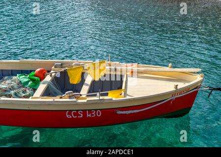 Parte di una piccola barca da pesca dipinta in rosso brillante, beige e verde nelle acque blu della costa mediterranea in una giornata di sole. Sono presenti padd Foto Stock