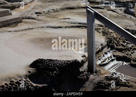 Scalini scolpiti sulla piattaforma rocciosa e un corrimano in legno, un paesaggio lunare terrestre bagnato che conduce alla piscina oceanica di Maroubra Foto Stock