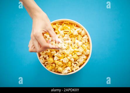 Cibo. Donna Mano che Prende Popcorn dal secchio. Benna Per Popcorn Su Sfondo Blu. Cinema Foto Stock