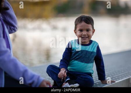 Un bambino di età felice di giocare con la sua sorella mentre si siede sulle banchine vicino ad un lago. Foto Stock