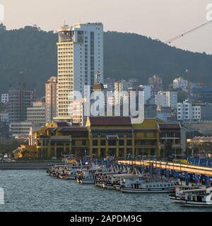 Una funivia passa su una fila di barche Junk mentre scende in Bai Chay, Hạ Long, Vietnam, proprio come il sole sta tramontando. Foto Stock