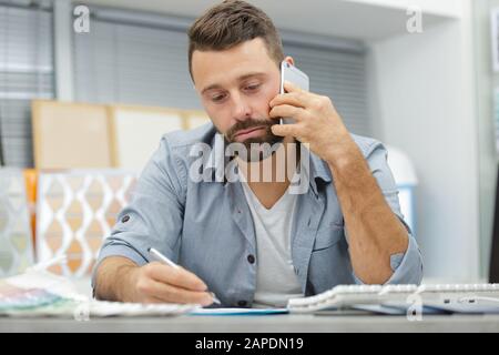 lavoratore maschile che parla con il cliente sullo smartphone Foto Stock
