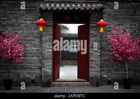 Porta e porta rossa che danno ingresso a un cortile privato e una casa di abitazione in un vicolo hutong a Pechino, Cina. Decorato per il Capodanno Cinese Foto Stock