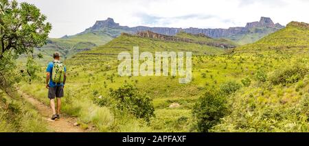 Un uomo escursionistico che gode del panorama dell'Anfiteatro e del Casco Di Polizia di formazione rocciosa, montagne Drakensberg, Parco Nazionale reale Natal, Foto Stock