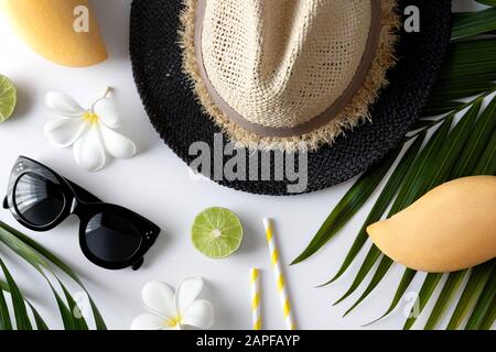 Composizione estiva con frutta, cappello, foglia di palma tropicale e fiori su sfondo bianco Foto Stock