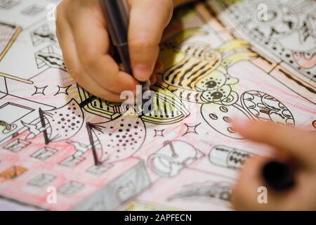 Profondità di campo poco profonda (fuoco selettivo) e immagine macro con la mano di una bambina che usa una sharpie per disegnare su un libro da colorare. Foto Stock