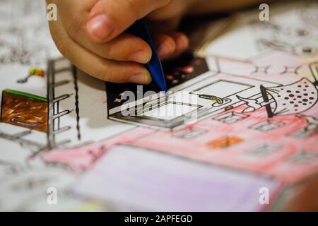 Profondità di campo poco profonda (fuoco selettivo) e immagine macro con la mano di una bambina che usa una matita per disegnare su un libro da colorare. Foto Stock