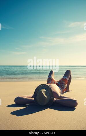 Silhouette di un uomo irriconoscibile che indossa un cappello di paglia che si rilassa sulla sabbia liscia di una spiaggia vuota Foto Stock