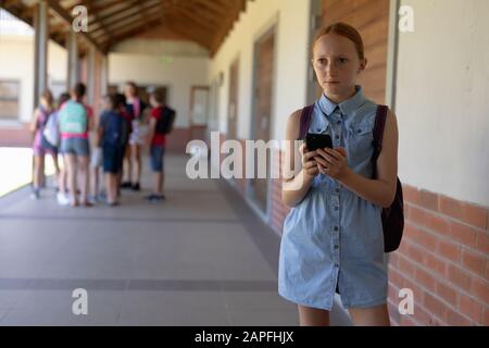 scolaretta che si trova nel cortile della scuola elementare usando uno smartphone Foto Stock