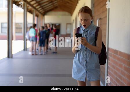 scolaretta che si trova nel cortile della scuola elementare usando uno smartphone Foto Stock