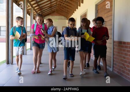 Gruppo di alunni che camminano in un corridoio esterno della scuola elementare Foto Stock