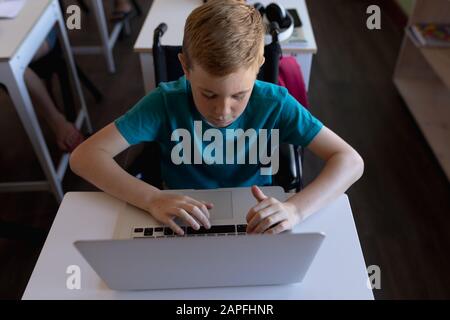 Schoolboy seduto alla scrivania con un computer portatile Foto Stock