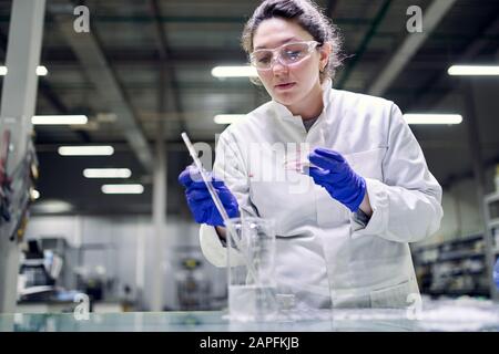 Una giovane donna di laboratorio seria in occhiali e pietri nelle sue mani conduce esperimenti su sfondo defocused Foto Stock