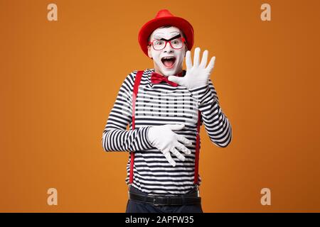 Happy mime in gilet e cappello rosso su sfondo arancione vuoto Foto Stock