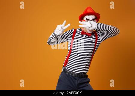 MIME in guanti bianchi e cappello rosso che guarda la fotocamera su sfondo arancione vuoto Foto Stock