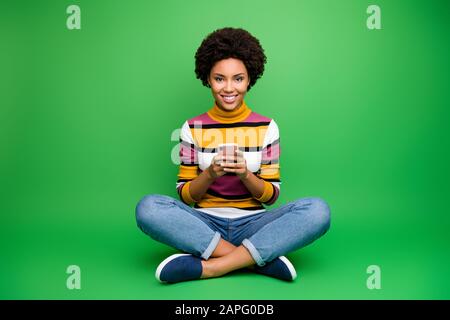 Foto completa del corpo di positivo afro americano ragazza blogger Sit gambe incrociate piegato utilizzare smartphone leggere social network notizie chill chat indossare brillare vestito Foto Stock