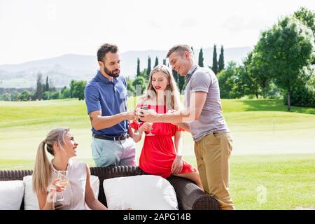 Gli amici si godono il vino e parlano sul divano sul campo da golf Foto Stock