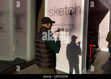 Un uomo parla al suo telefono utilizzando la funzione vivavoce, in un angolo soleggiato vicino a 'Sketch', una gastro-galleria su Conduit Street, il 20th gennaio 2020, a Londra, Inghilterra. Foto Stock