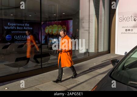 Un uomo che indossa un cappotto orgge cammina oltre la finestra dell'ufficio Qatar Airlines su Conduit Street a Mayfair, il 20th gennaio 2020, a Londra, Inghilterra. Foto Stock