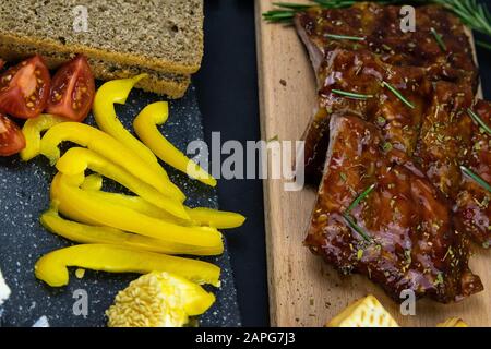 Costolette sotto salsa al miele su un pannello di legno accanto a pomodori, pane e carta campana. Viste dall'alto Foto Stock