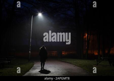 Pedonale femmina isolato di notte sotto la lampada da strada del Regno Unito. Lone figura nel buio. Foto Stock