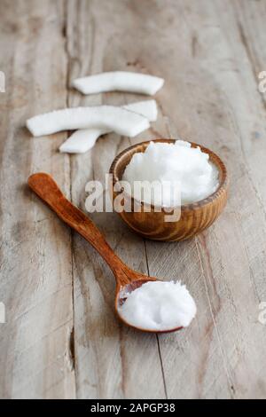 Olio di noce di cocco in una ciotola di legno con un cucchiaio di legno vicino fino Foto Stock