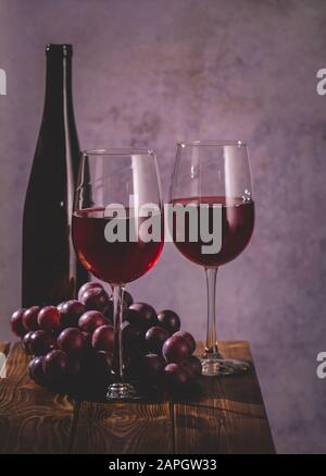 Due bicchieri di vino rosso con uva e bottiglia di vino su un tavolo di legno Foto Stock