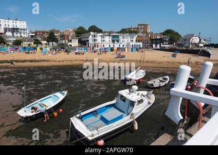 Le persone che si crogiolano al sole sulla spiaggia e le barche da diporto e da pesca nel porto di Viking Bay, Broadstairs, Kent, Regno Unito Foto Stock