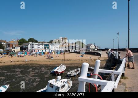 Le persone che si crogiolano al sole sulla spiaggia e le barche da diporto e da pesca nel porto di Viking Bay, Broadstairs, Kent, Regno Unito Foto Stock