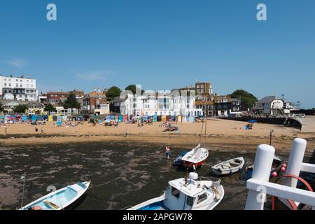 Le persone che si crogiolano al sole sulla spiaggia e le barche da diporto e da pesca nel porto di Viking Bay, Broadstairs, Kent, Regno Unito Foto Stock