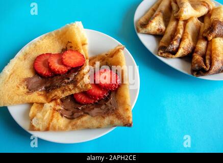 Frittelle dolci fresche con pasta di cioccolato e fragola su sfondo blu brillante. Frittelle di stile russo per la settimana Pancake. Frittelle inglesi avvolte. Foto Stock