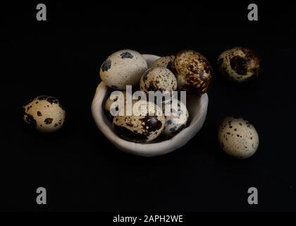 Dieci uova di quaglia non lavate in vaso di ceramica bianca su sfondo nero e copia-spazio, vista dall'alto Foto Stock