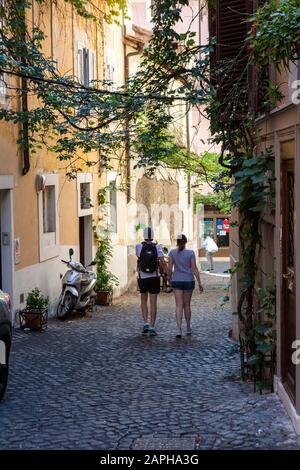 Giovane coppia in vacanza a piedi a mano in giù una tranquilla strada lastricata laterale con viti che crescono sulle mura di Roma Foto Stock
