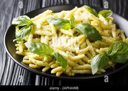 Pasta tradizionale trofie con pesto di basilico verde e parmigiano da vicino in un piatto sul tavolo. Orizzontale Foto Stock