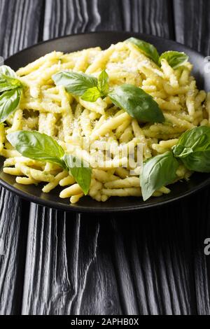 Pasta trofie preparata di fresco con pesto di basilico e parmigiano da vicino in un piatto sul tavolo. Verticale Foto Stock