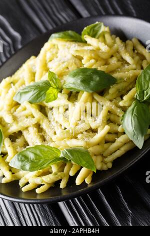 Trofie alimentare italiana con pesto di basilico e parmigiano da vicino in un piatto sul tavolo. Verticale Foto Stock