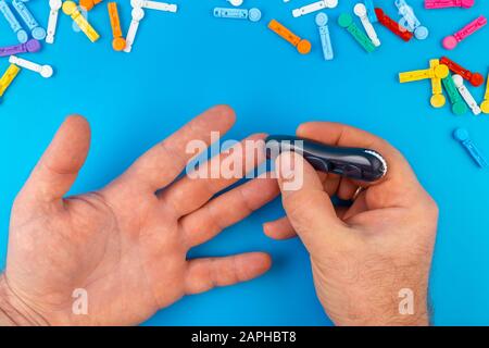 Test sul diabete. L'uomo le mani che controllano il livello di zucchero di anima da glucometro su fondo blu. Un dispositivo per la misurazione dei livelli di zucchero nel sangue. Strisce di prova, pillole Foto Stock