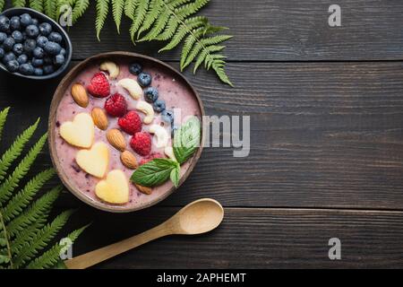 Una sana colazione tropicale banana e mirtillo smoothie decorate con frutti nella tazza di cocco sulla tavola di legno. Vista da sopra. Pulire mangiare, vegetar Foto Stock