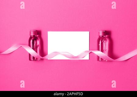 Disposizione piatta di due piccole bottiglie mockup con prodotti cosmetici spa su sfondo rosa brillante e carta bianca isolata. Donna bellezza e salone di bellezza cosmet Foto Stock