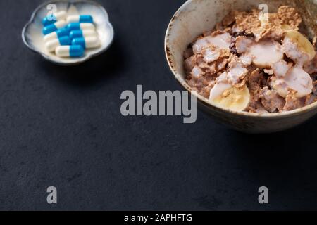 Ciotola di granola con yogurt e banana e supplementi sportivi su sfondo di pietra scura. Primo piano. Spazio di copia. Foto Stock