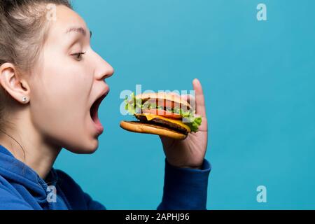 La ragazza ha aperto la sua bocca larga e sta andando mangiare un hamburger, vista laterale Foto Stock