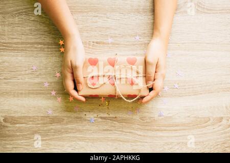 Scatola regalo avvolta con carta marrone artigianale con cuori in mani femminili, dando concetto Foto Stock